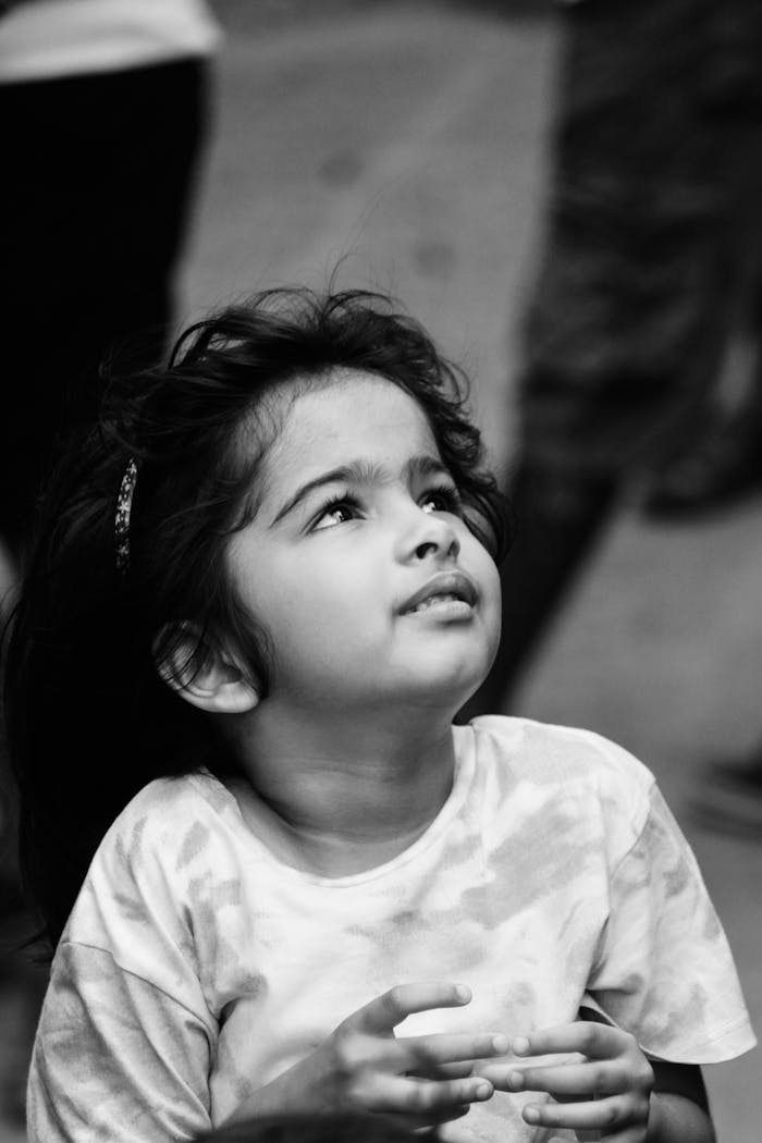 A captivating black and white portrait of a young girl gazing upwards with an expression of wonder.