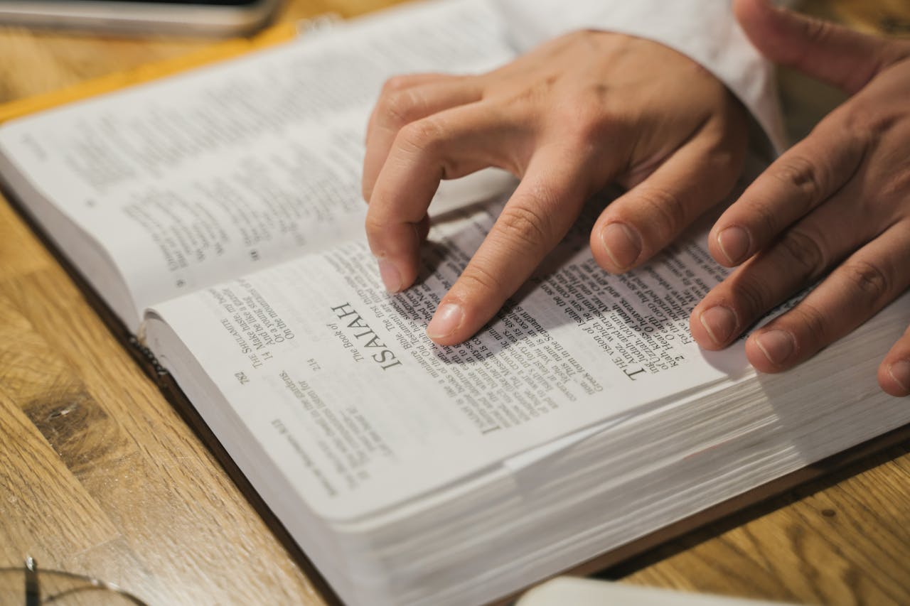 services-02 Close-up of hands reading a Bible, focusing on Isaiah passage, in an intimate indoor setting.